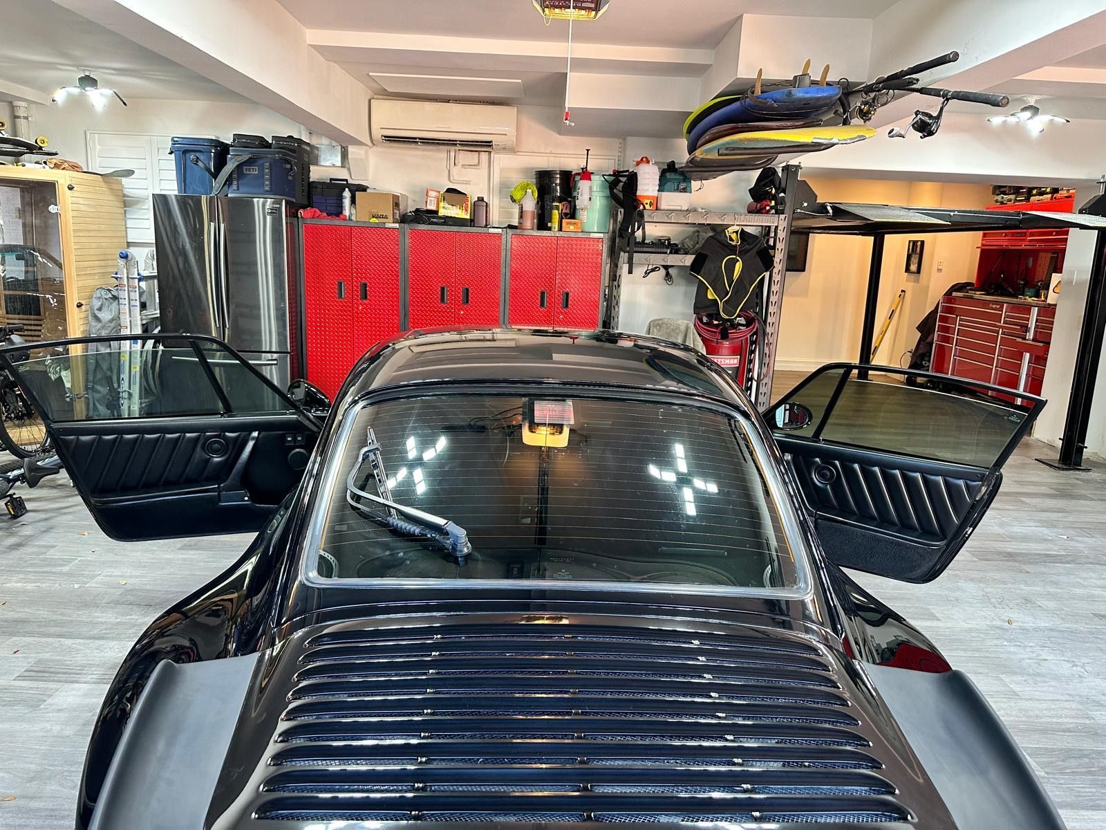 A black sports car is parked in a garage with its doors open.