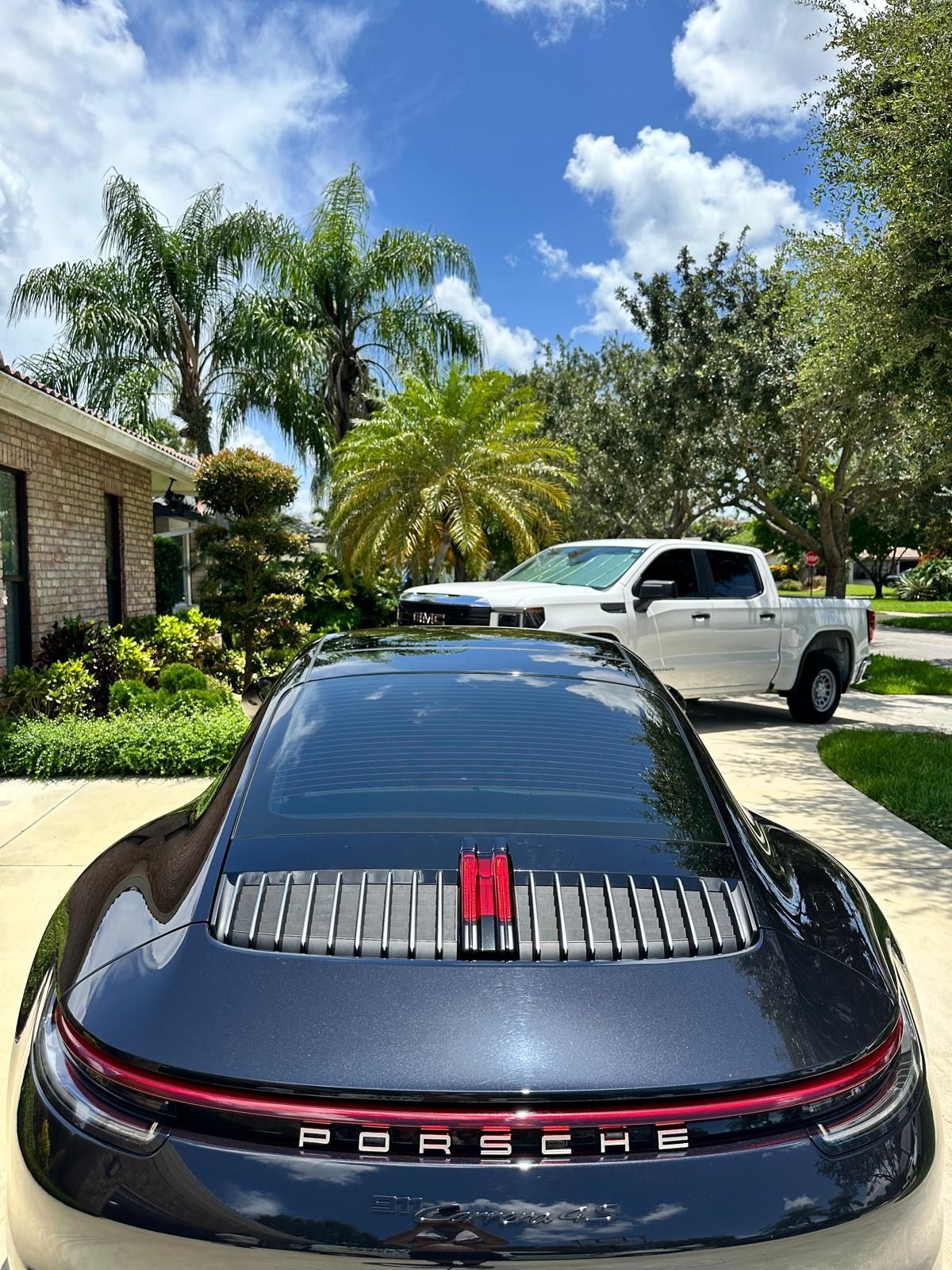 A black porsche 911 is parked in a driveway next to a white truck.