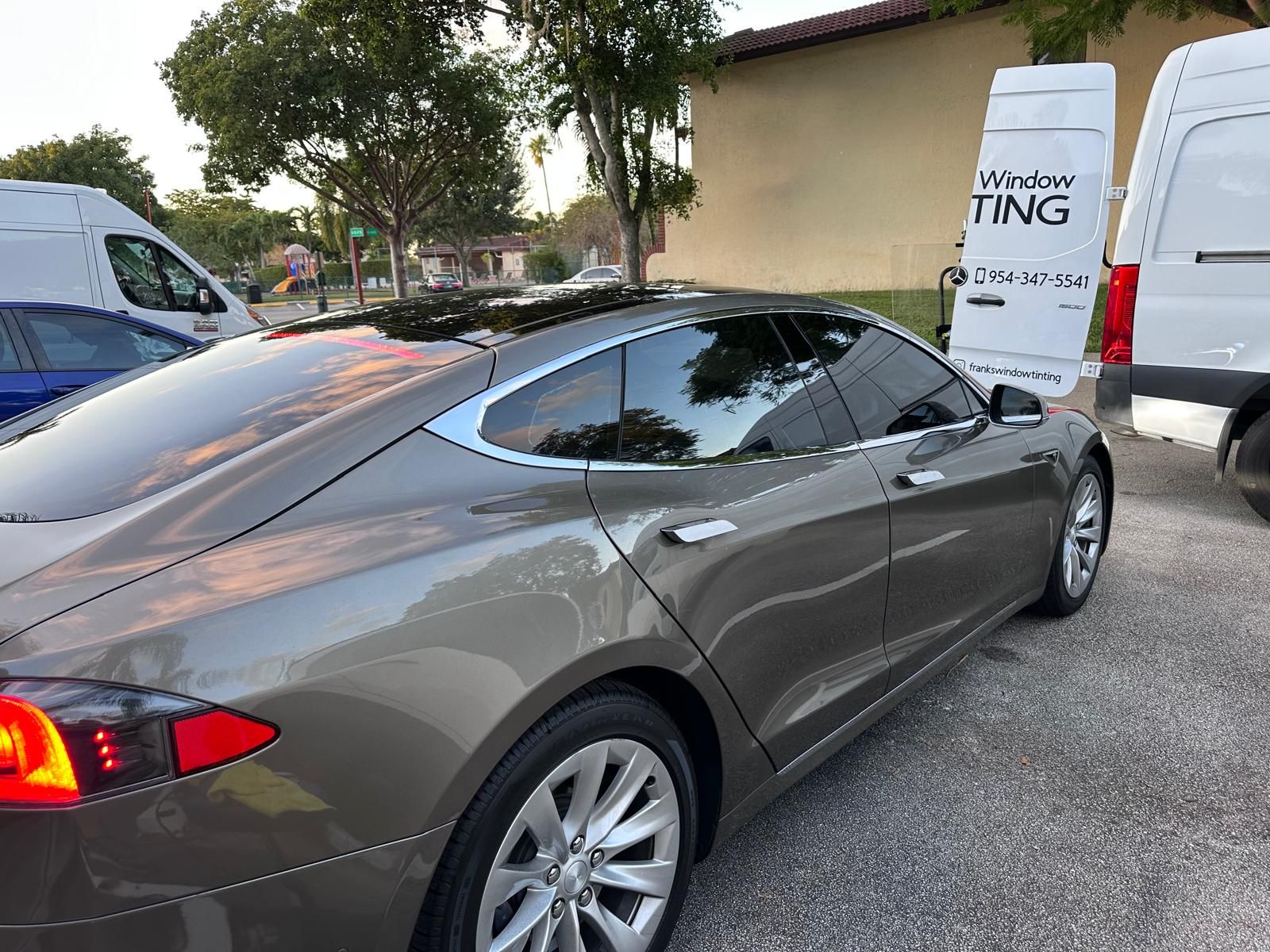 A tesla model s is parked in a parking lot next to a van.