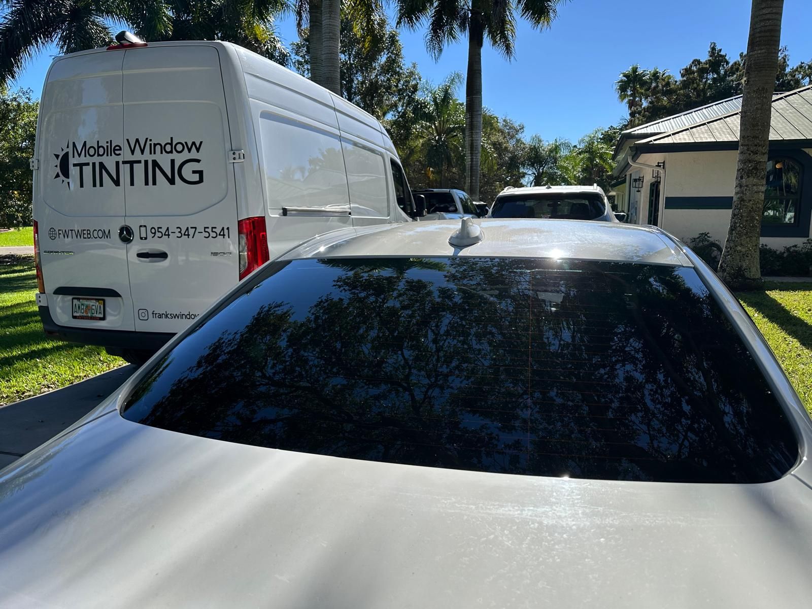 A car is parked in front of a van that says mobile window tinting.