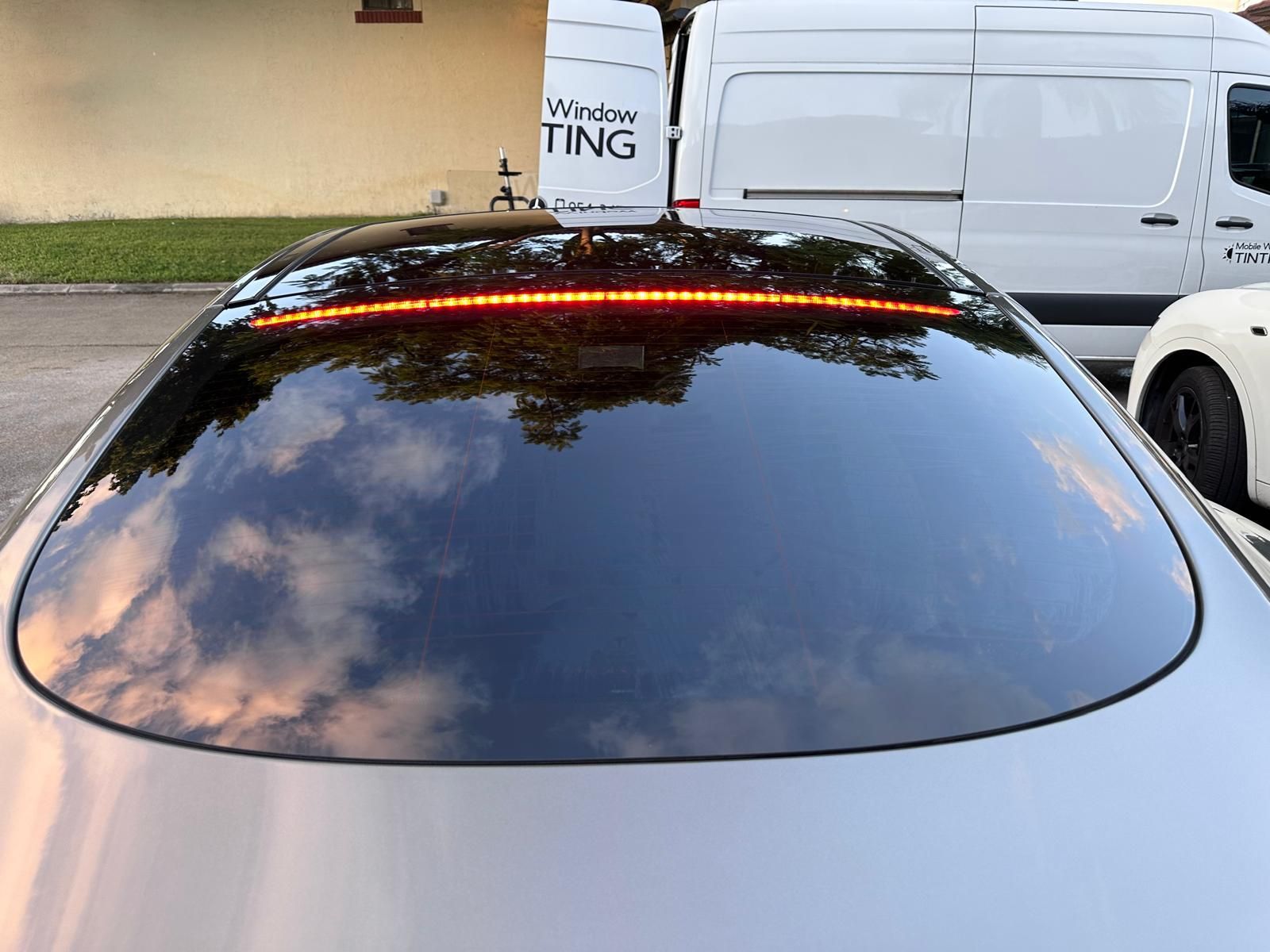 The rear window of a car with a reflection of trees in it.