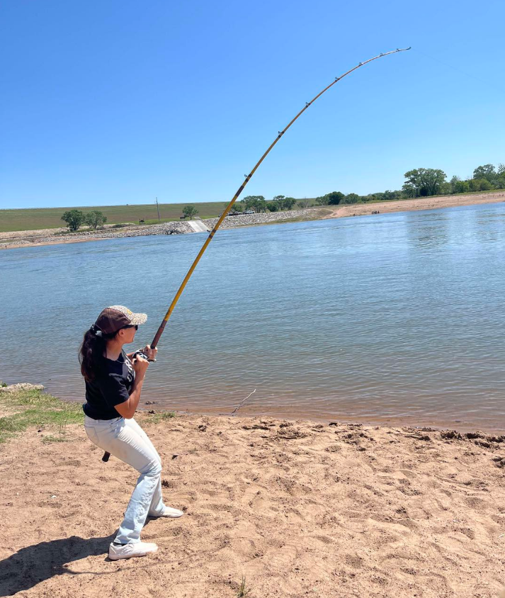 Woman fishing at a lake on a sunny day, holding a bent fishing rod, sandy shore.