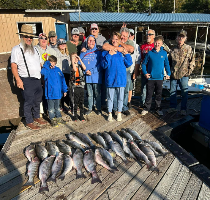 Group of people on dock with caught fish. Sunny day, blues, grays, and expressions of joy.