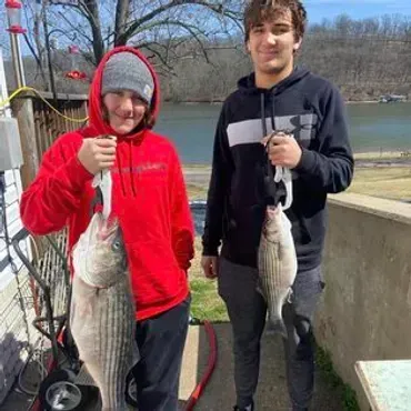 Two people holding up fish they caught outdoors near a body of water.