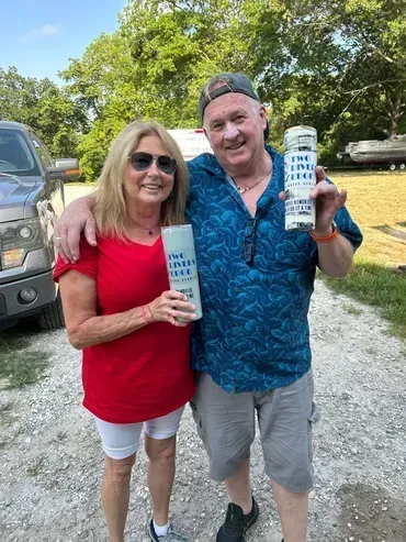 Woman in red shirt and man in blue shirt hold cylinders with text, outdoors.