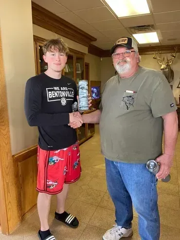 Two men shaking hands, one holding a beverage can. Interior shot with taxidermy on wall.