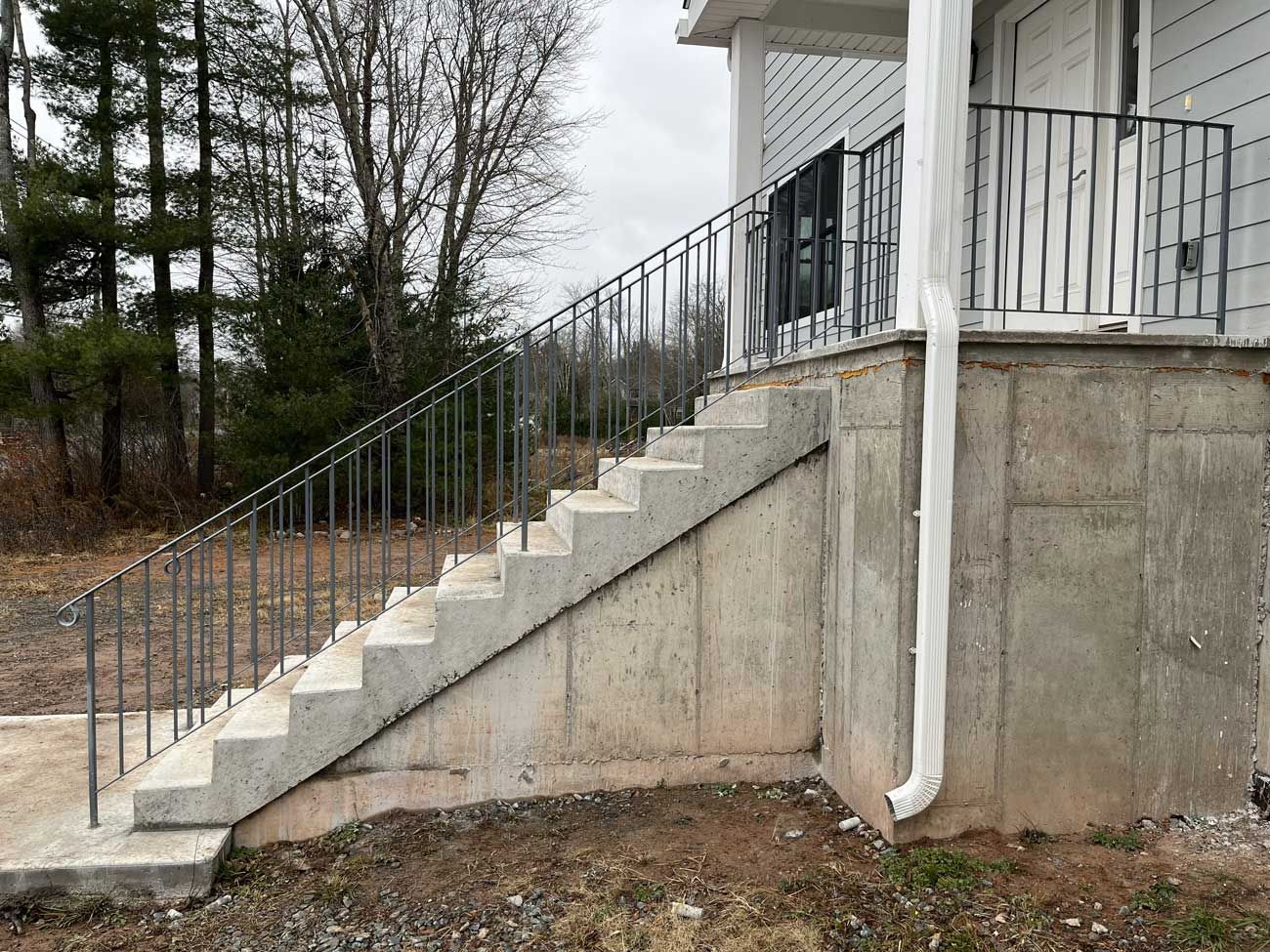 Concrete staircase with metal railing leading to a white building's porch, set outdoors with trees.