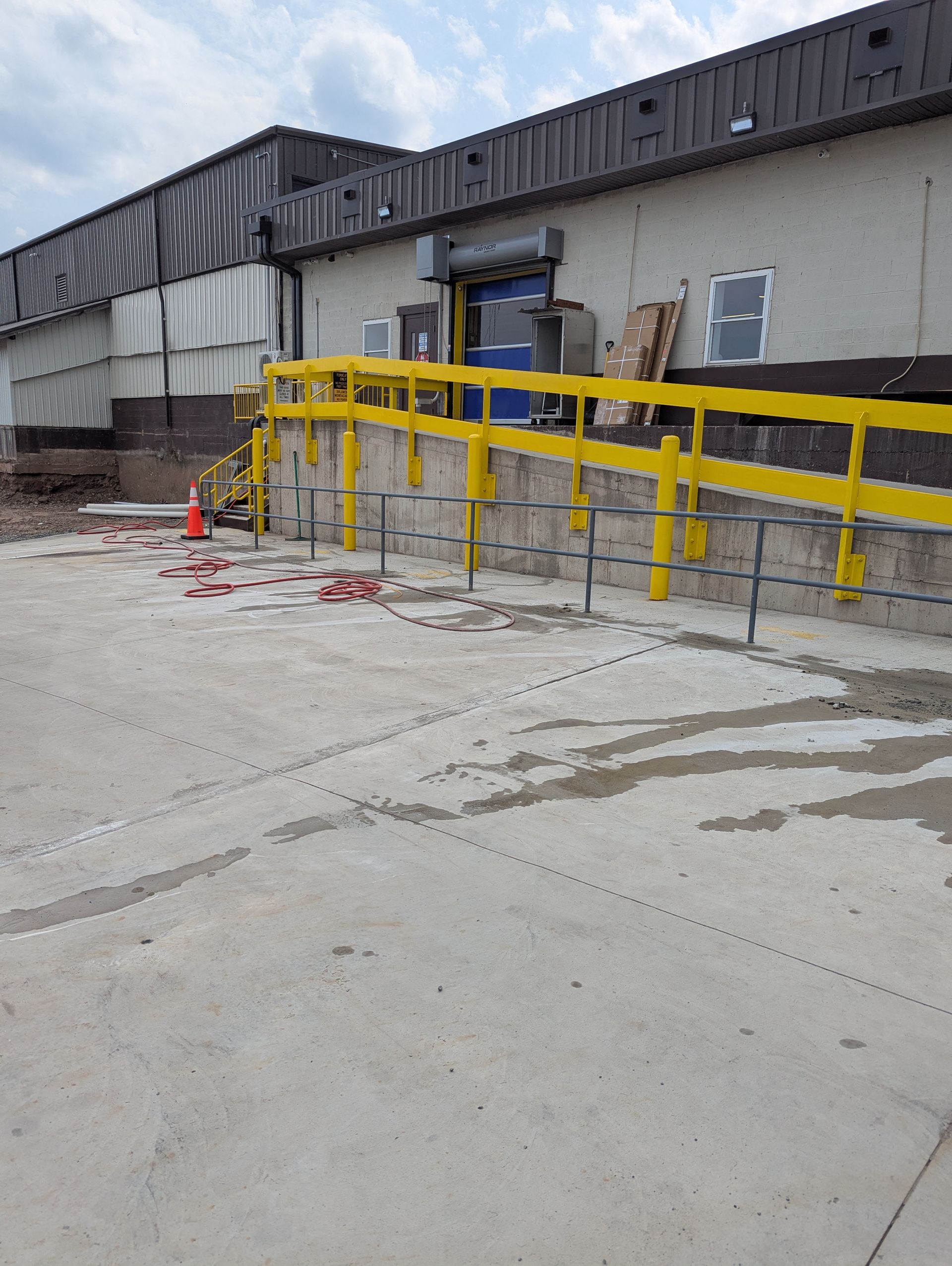 Yellow ramp with handrails leading up to a loading dock door. Concrete in foreground, brick and siding in background.