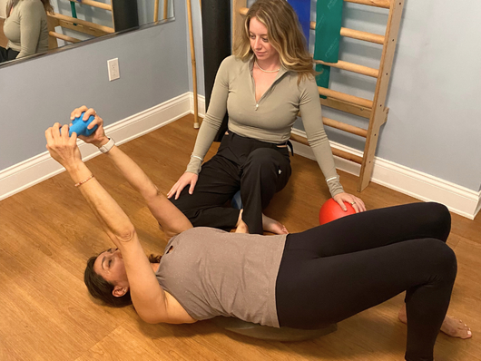 A woman is laying on the floor while another woman holds a ball.