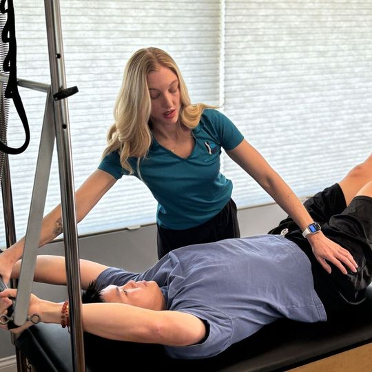 A woman is helping a man on a pilates machine