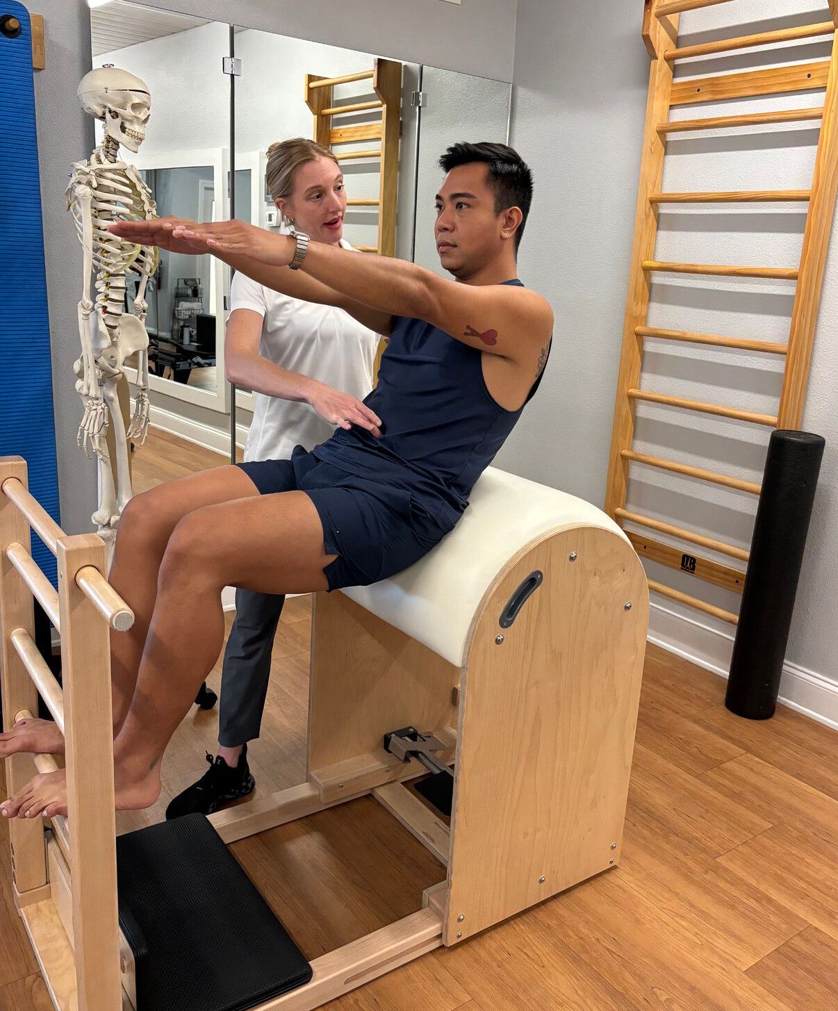 A man is doing exercises on a pilates machine while a woman looks on.