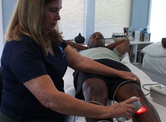 A woman is using a red light on a man 's leg