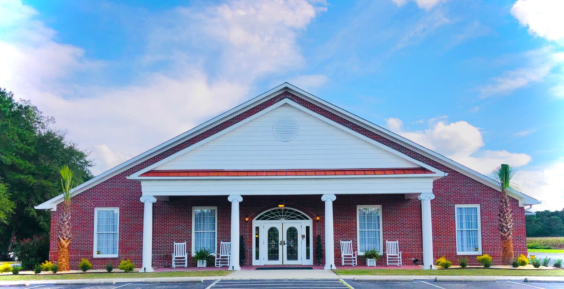 Brick building with white pillars, double doors, and a triangular roof under a blue sky.