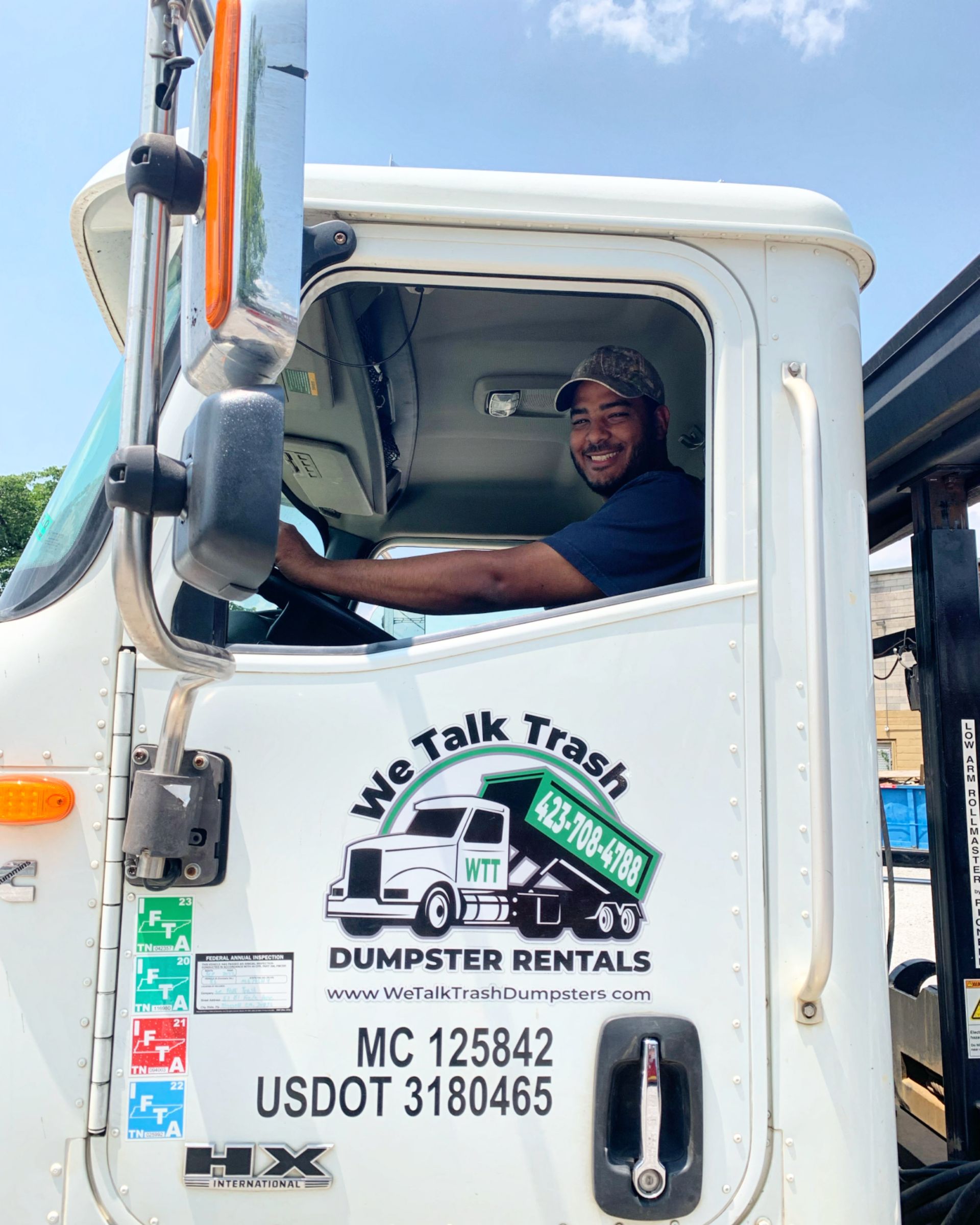 A man is sitting in the driver 's seat of a dumpster truck.