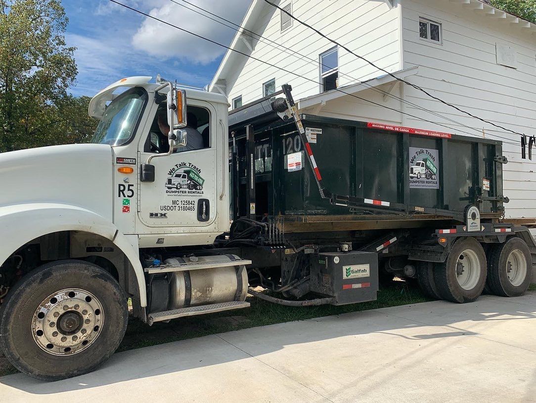 A dump truck is parked in front of a white house.