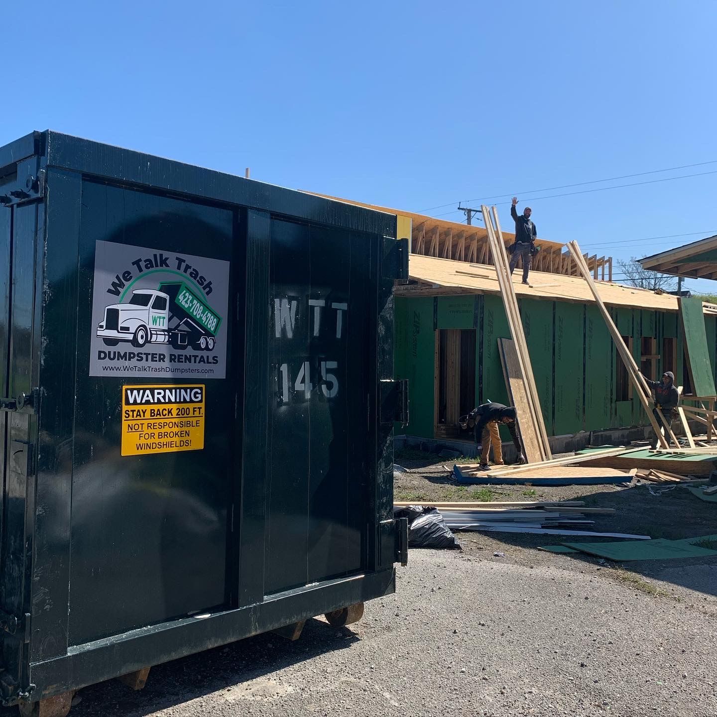 A dumpster is parked in front of a building under construction.