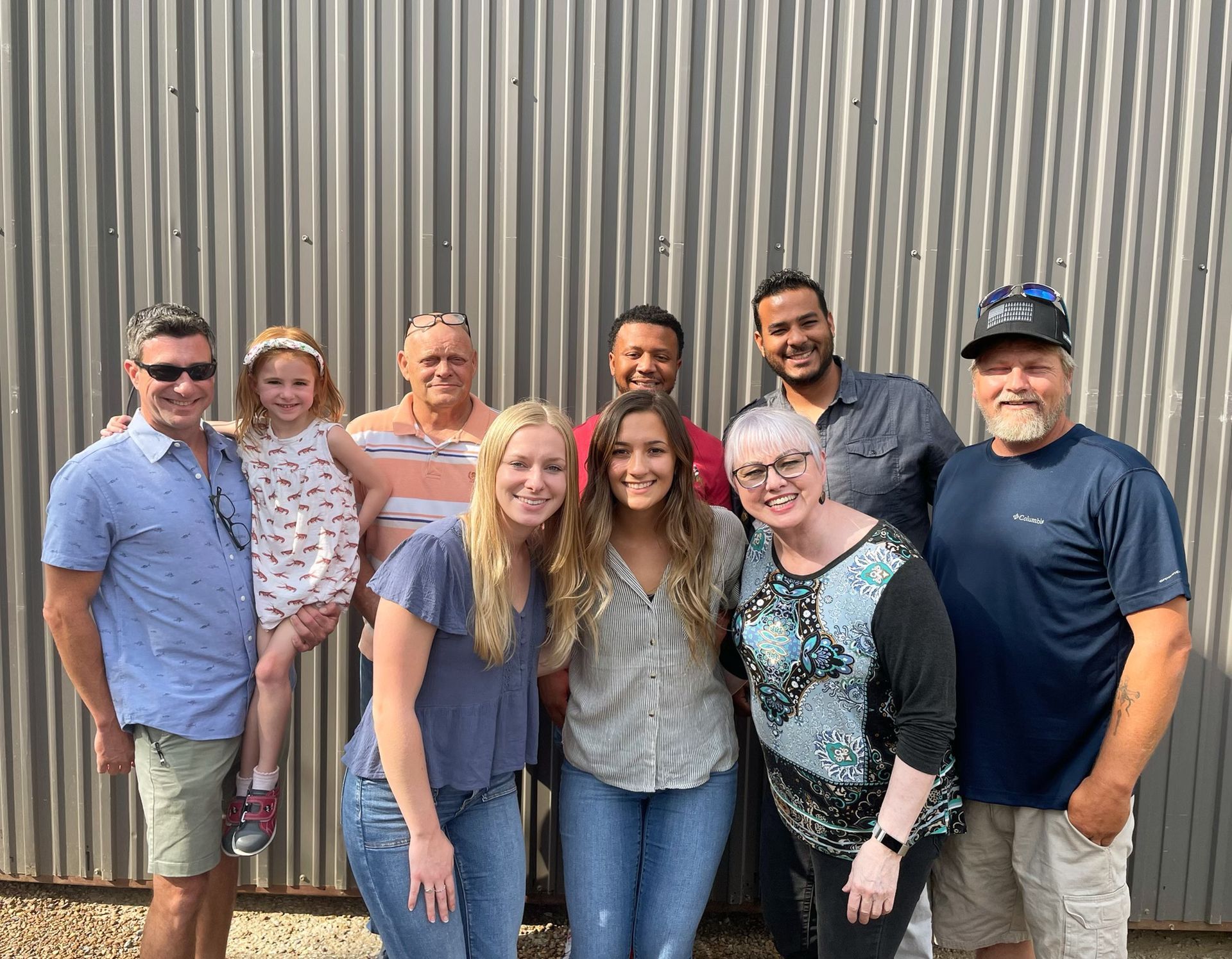 A group of people are posing for a picture in front of a metal wall.