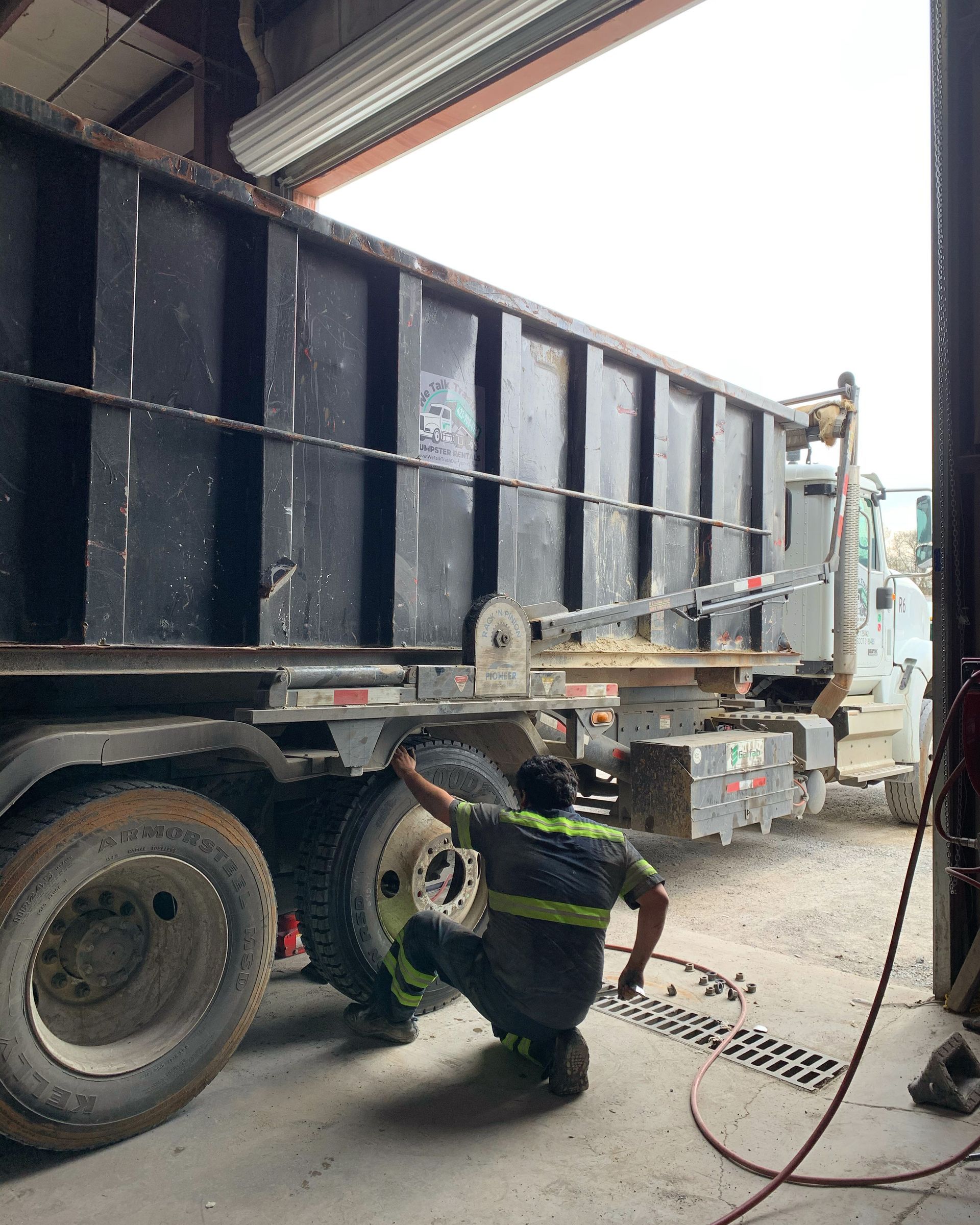 A man is kneeling next to a dump truck in a garage.
