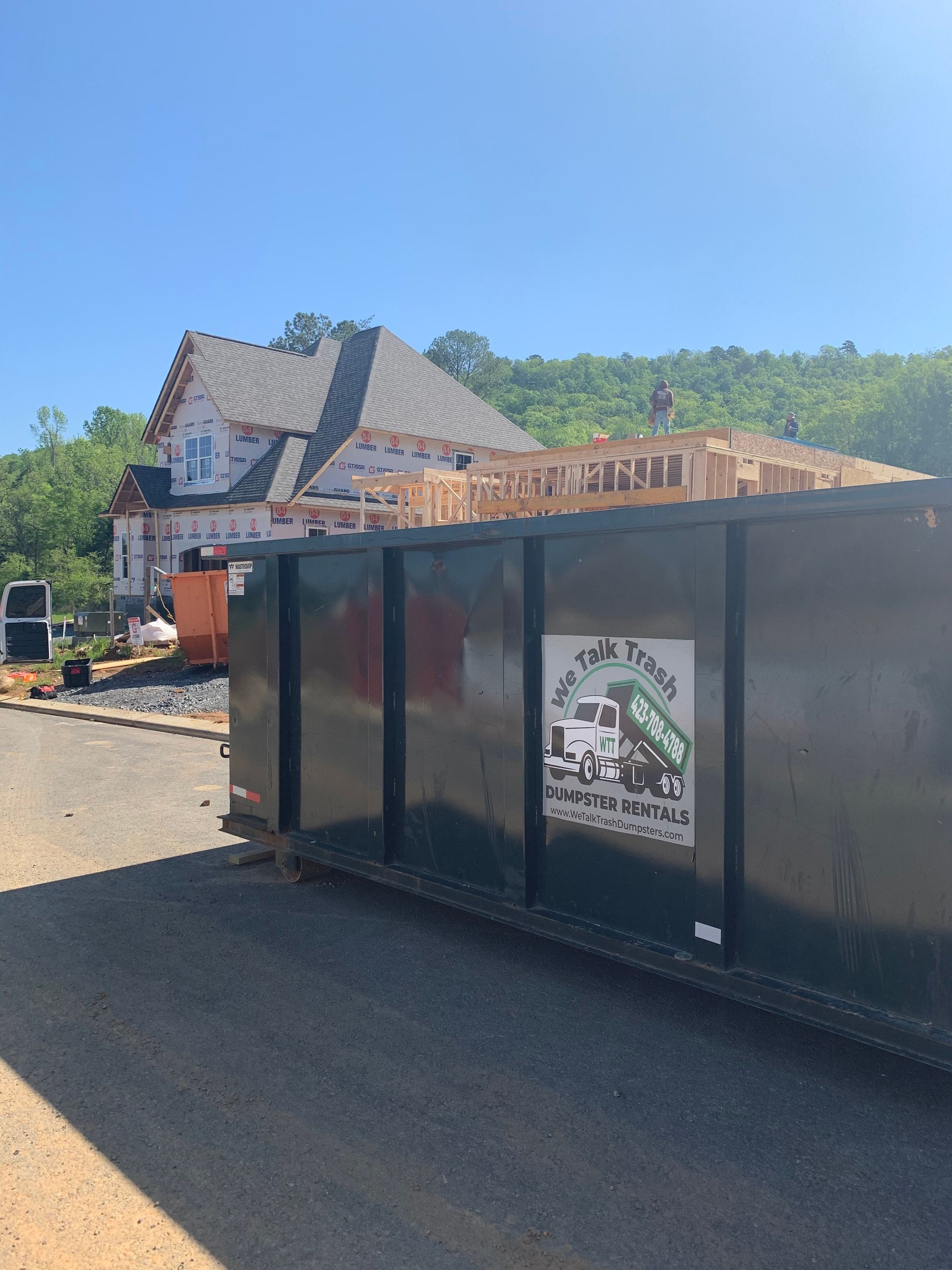 A large dumpster is parked in front of a house under construction.