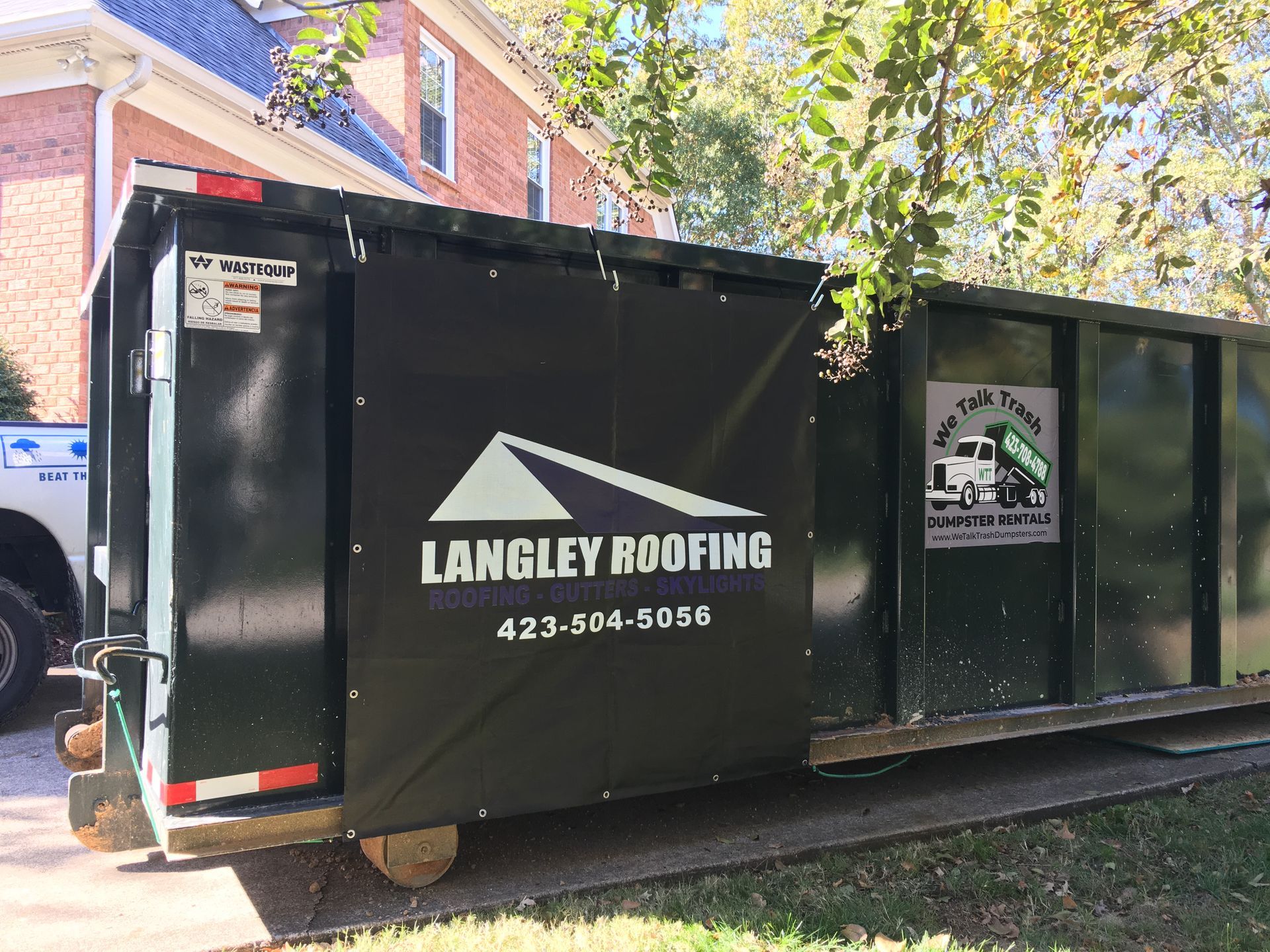A dumpster for langley roofing is parked in front of a house