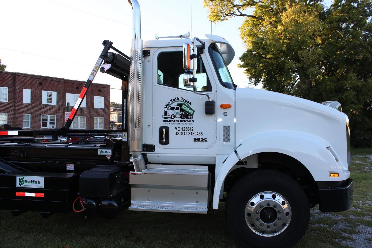 A white dump truck with the number 0 on the side is parked in a grassy field.