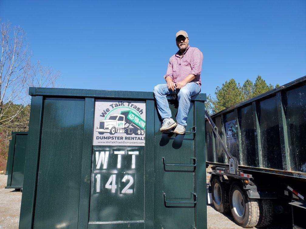 A man is sitting on top of a dumpster.