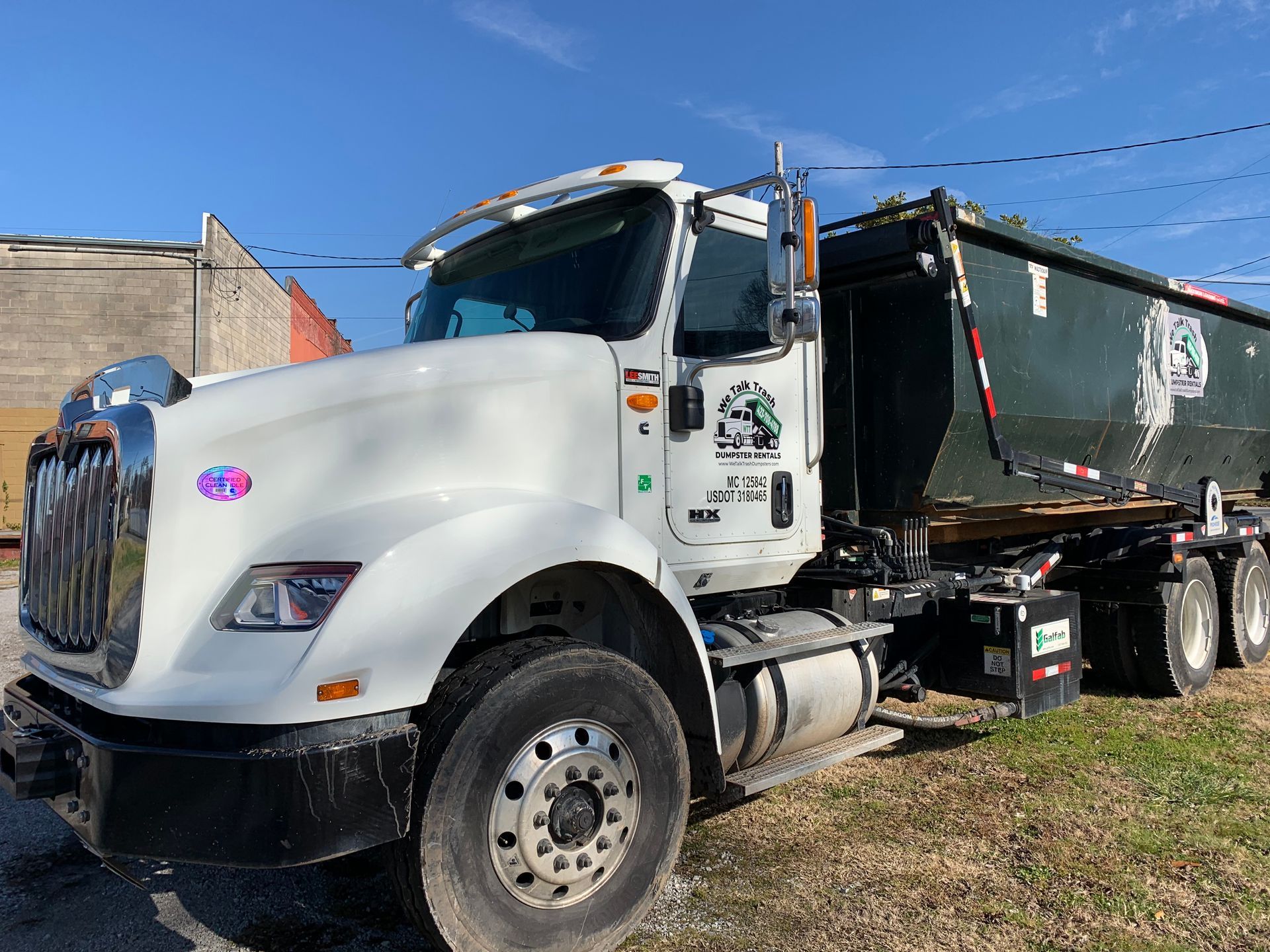 A white dump truck is parked in a grassy field.