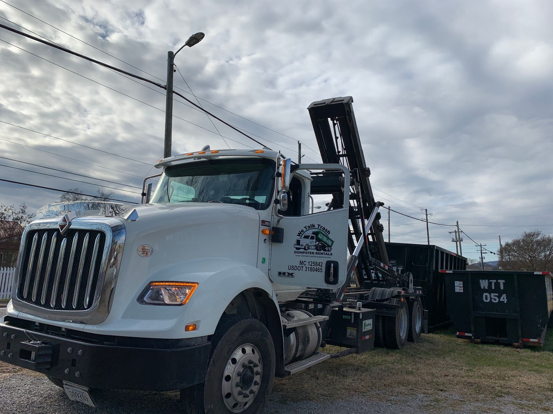 A large white dump truck is parked next to a black dumpster.