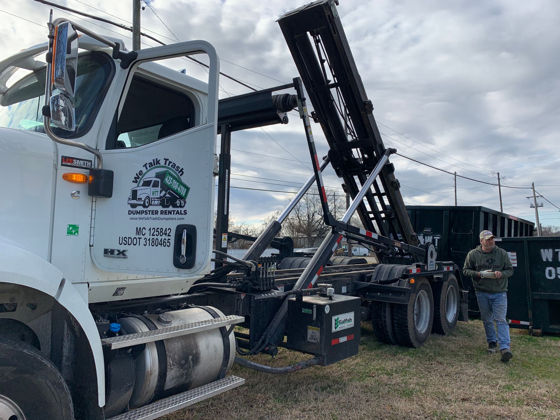 A man is standing next to a dump truck in a field.