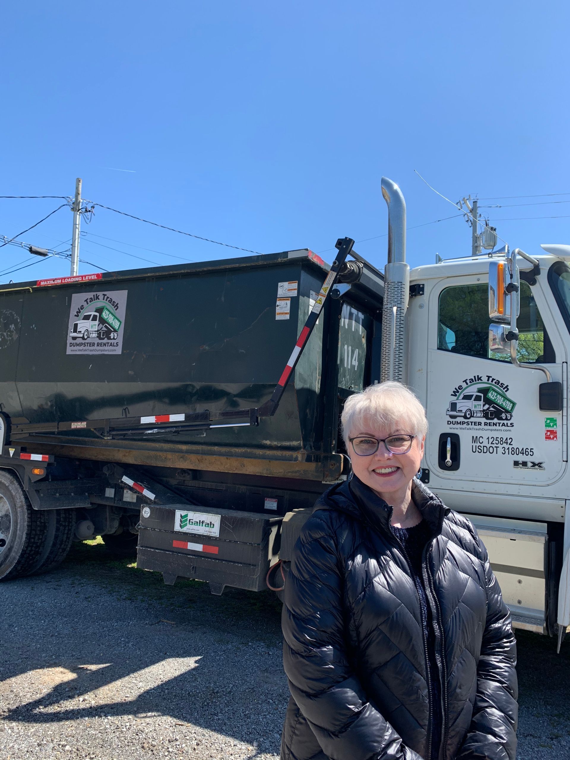 A woman is standing in front of a dumpster truck.
