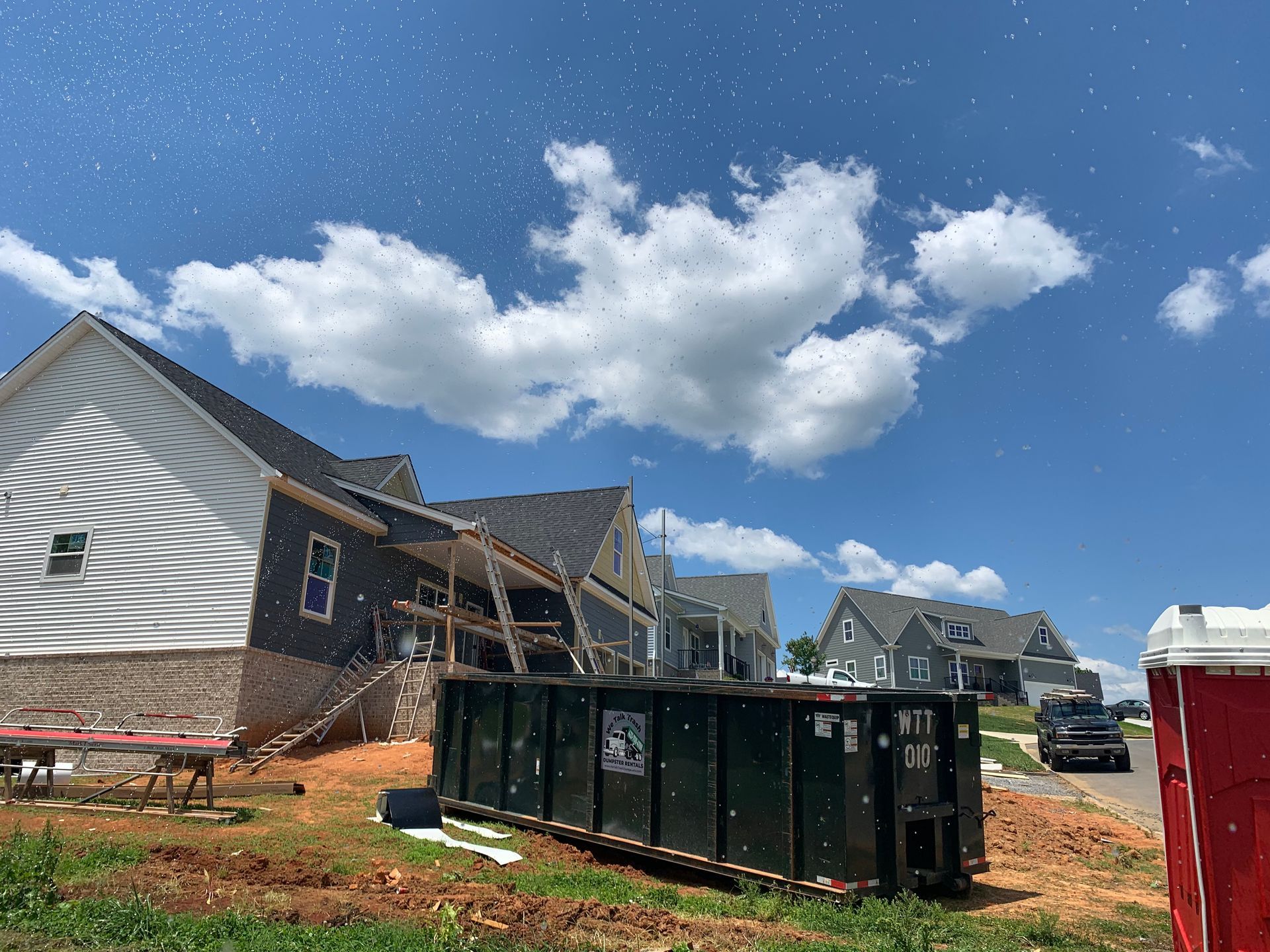 A dumpster is parked in front of a house under construction.