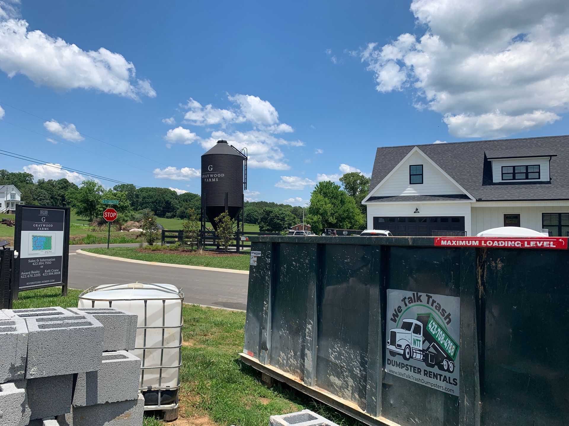 A dumpster with a truck on it is in front of a house