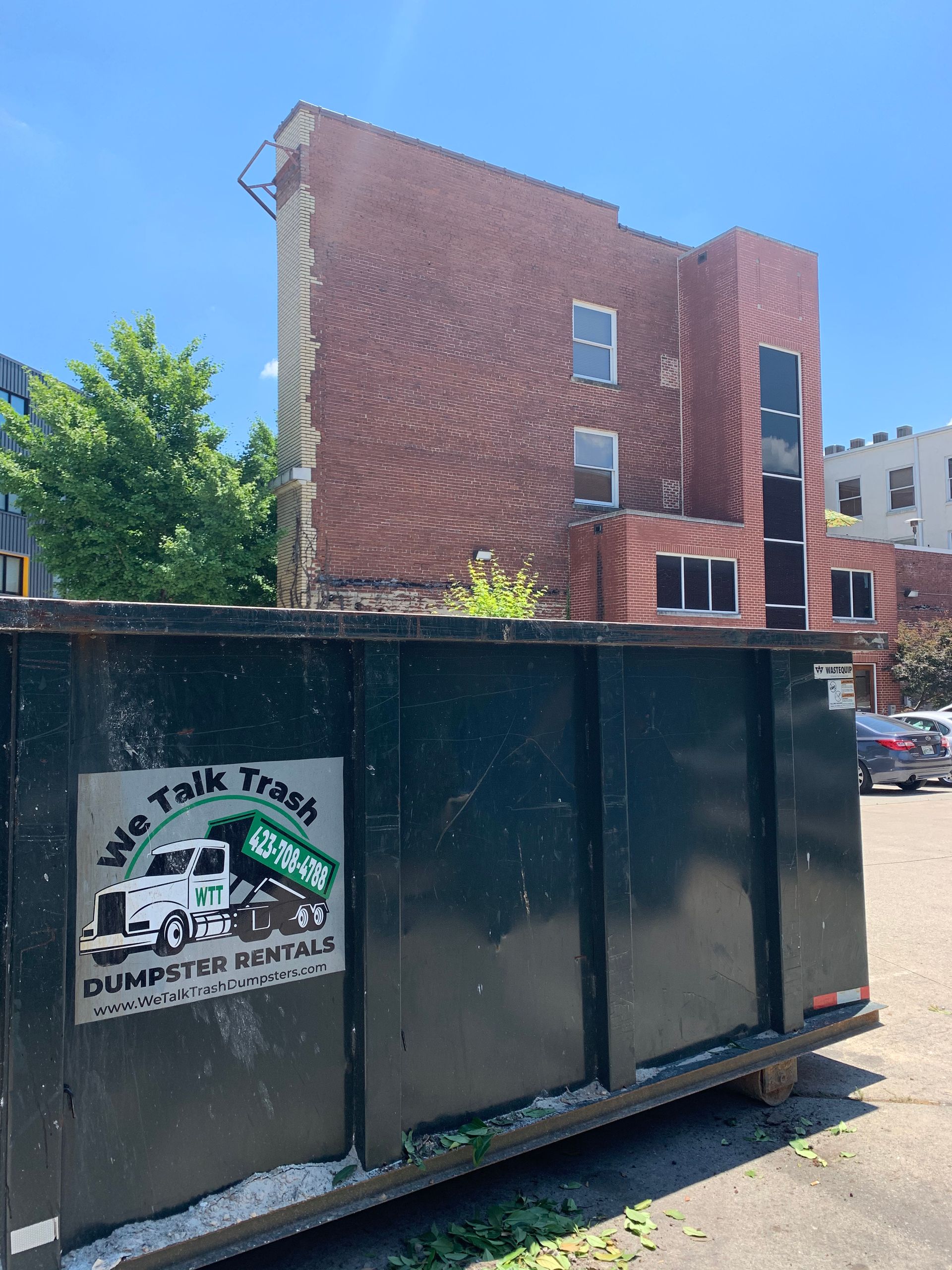 A dumpster is parked in front of a brick building.