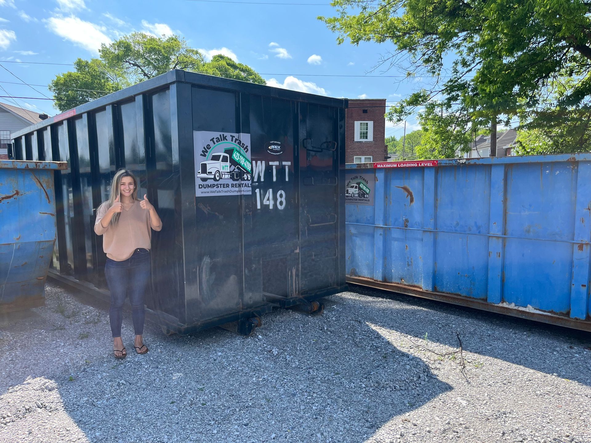 A woman is standing in front of a large dumpster.