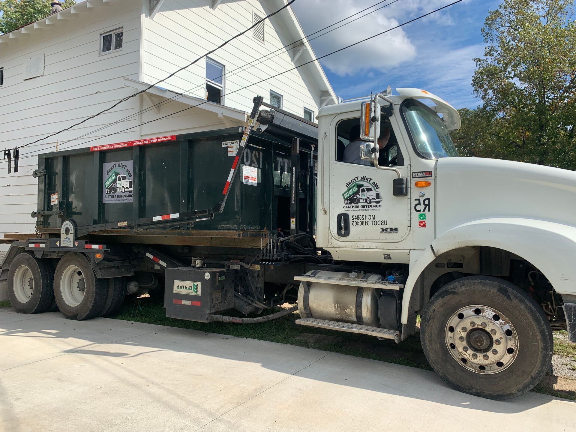 A dump truck is parked in front of a white house.