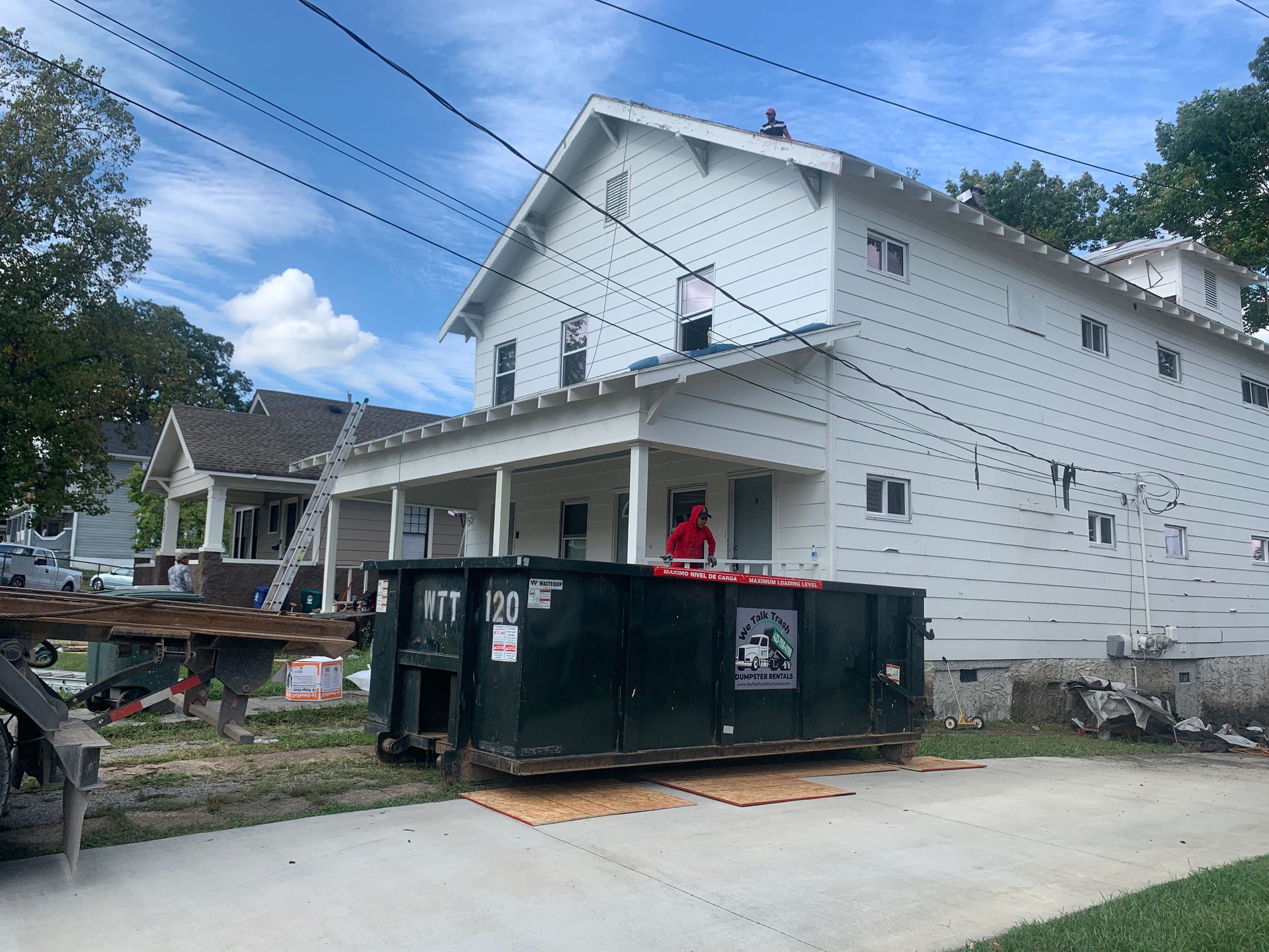 A dumpster is parked in front of a white house.