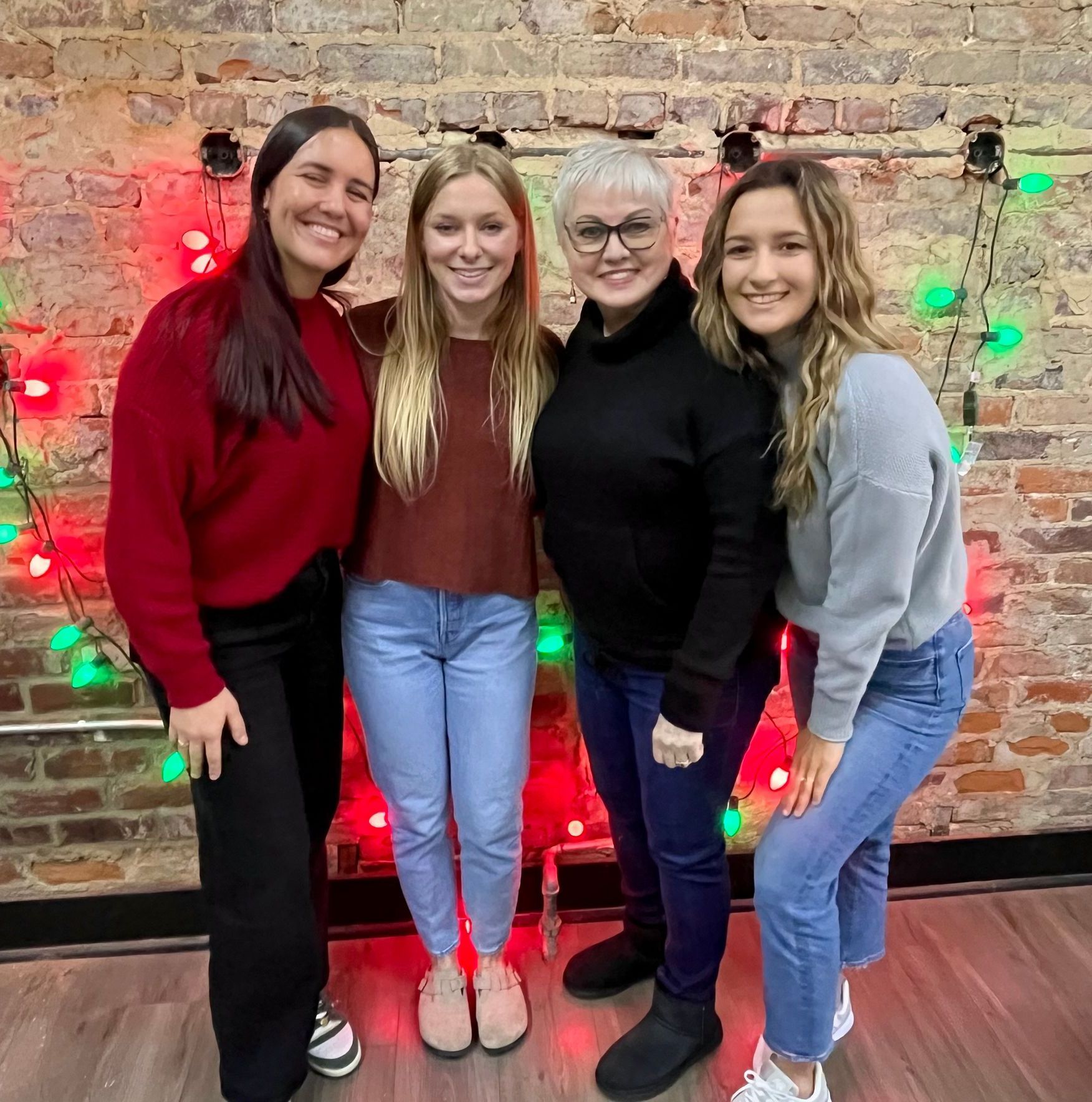 Four women are posing for a picture in front of a brick wall.