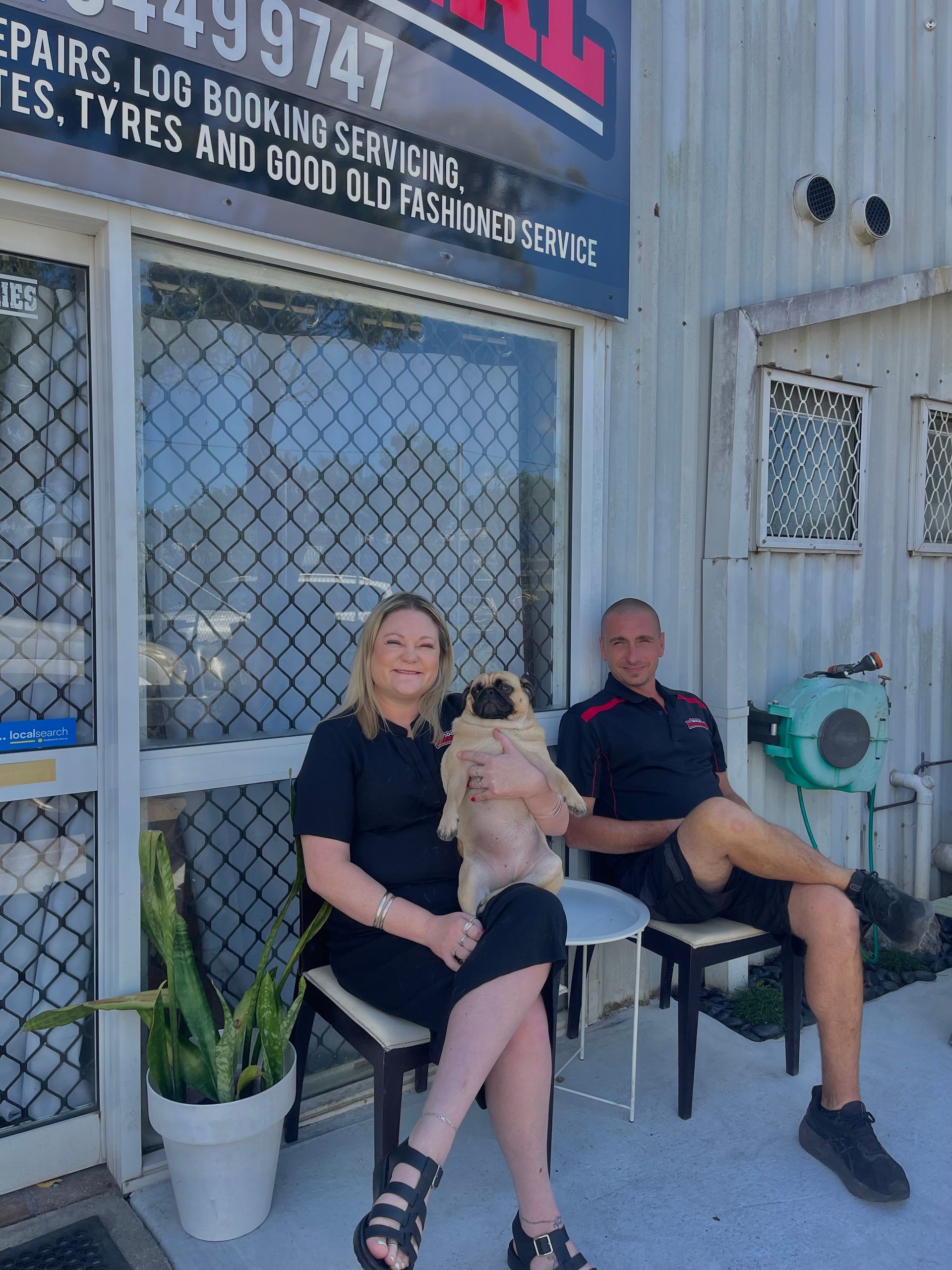 A man and a woman are sitting in front of a building holding a dog