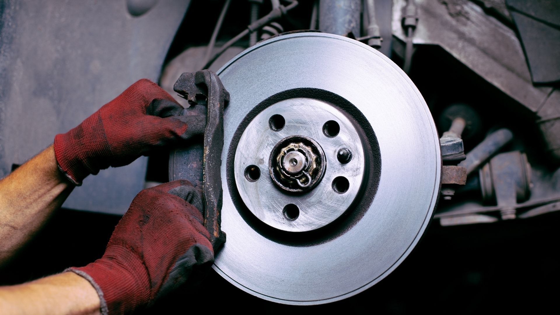 A person wearing red gloves is cleaning a brake disc