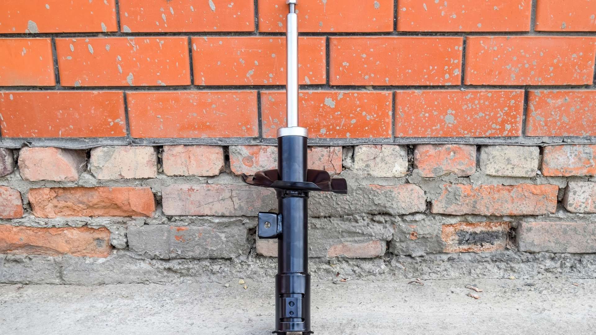 A shock absorber is sitting in front of a brick wall.