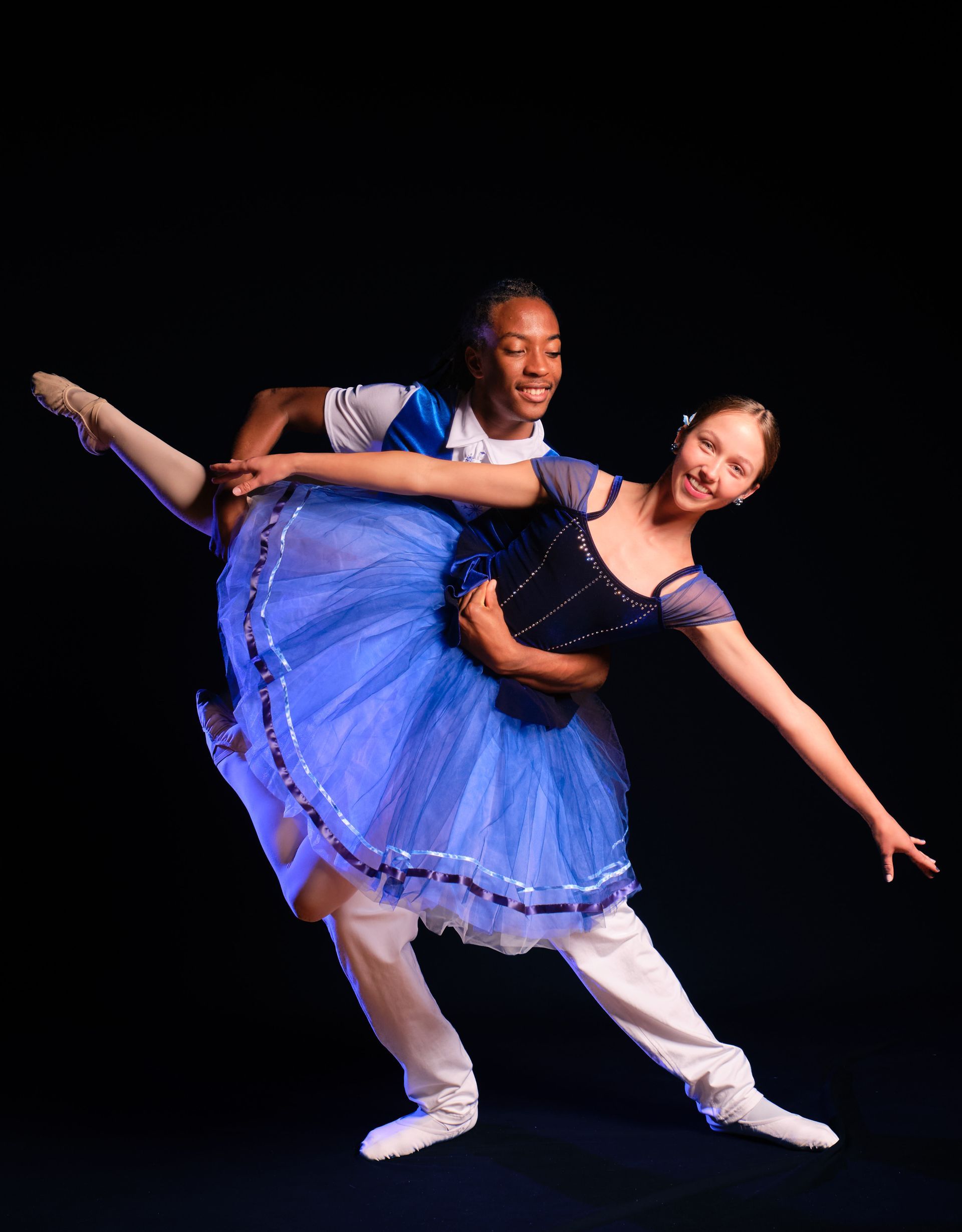 Two dancers in black tutus posing with arms raised in a bright studio