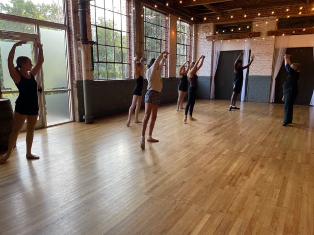 Children doing a playful dance class with arms raised in a bright studio