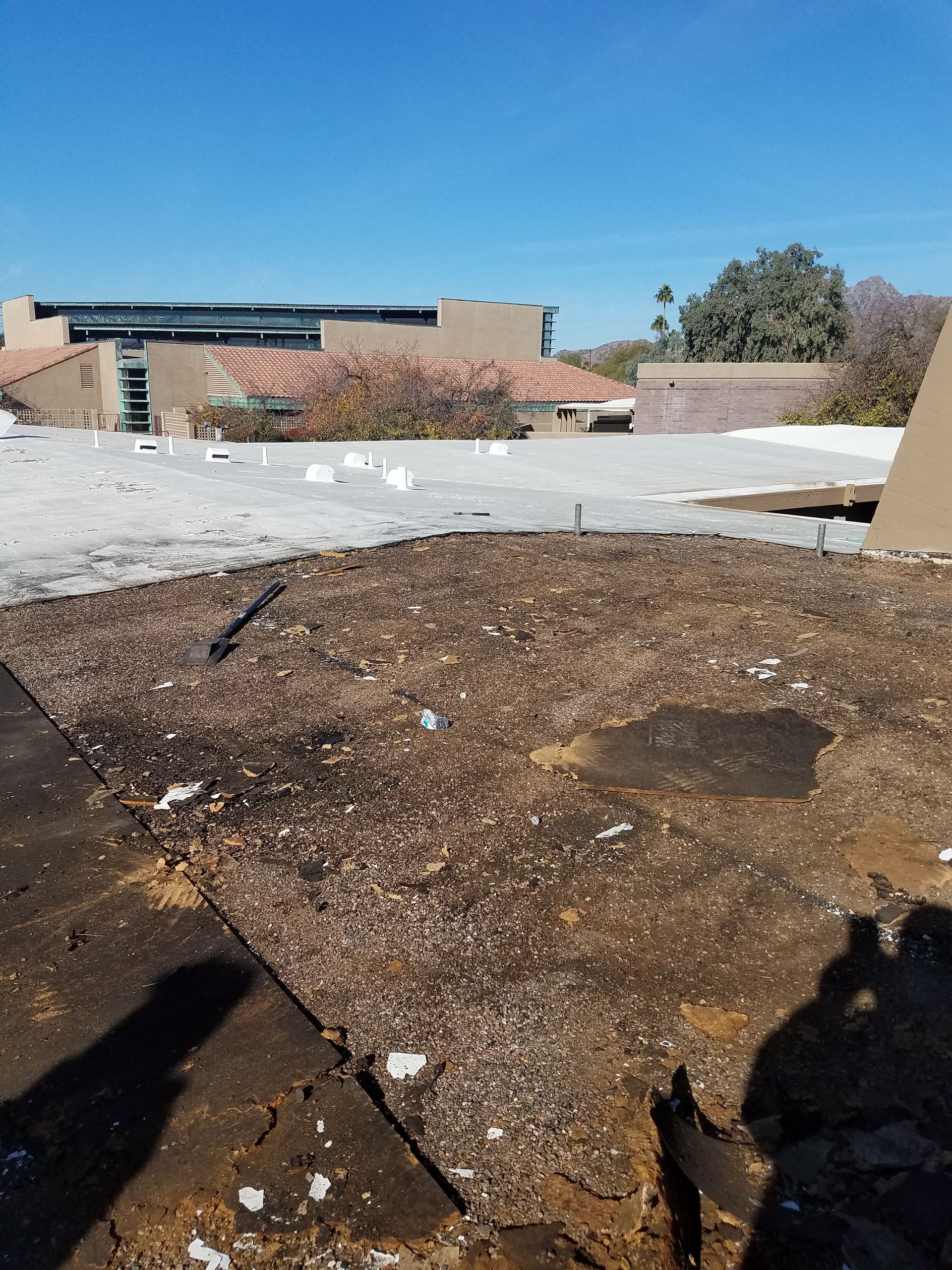 Rooftop with dark wet patch and debris under a blue sky, with buildings in the background