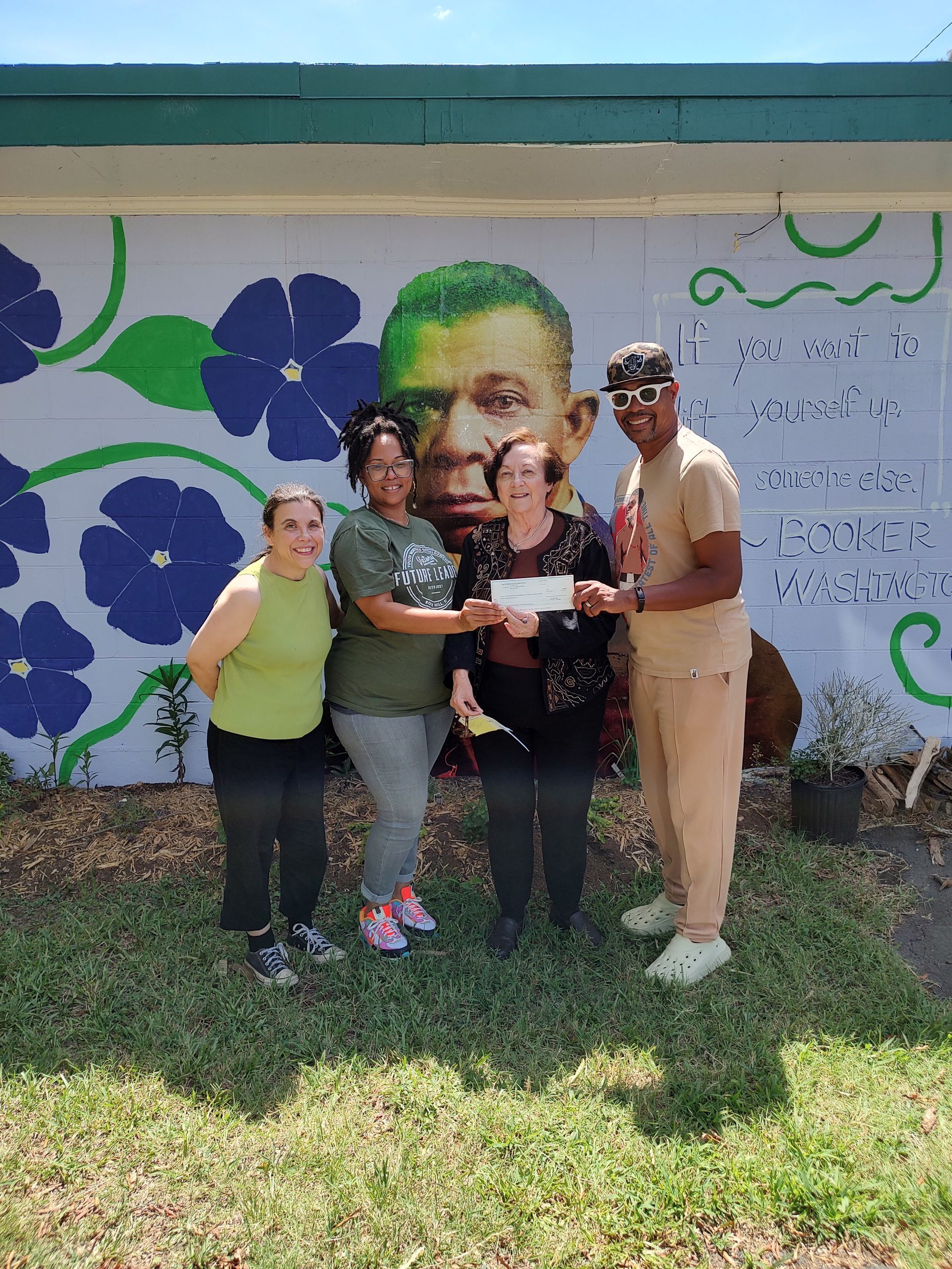 Group of four people pose with a check in front of a mural.