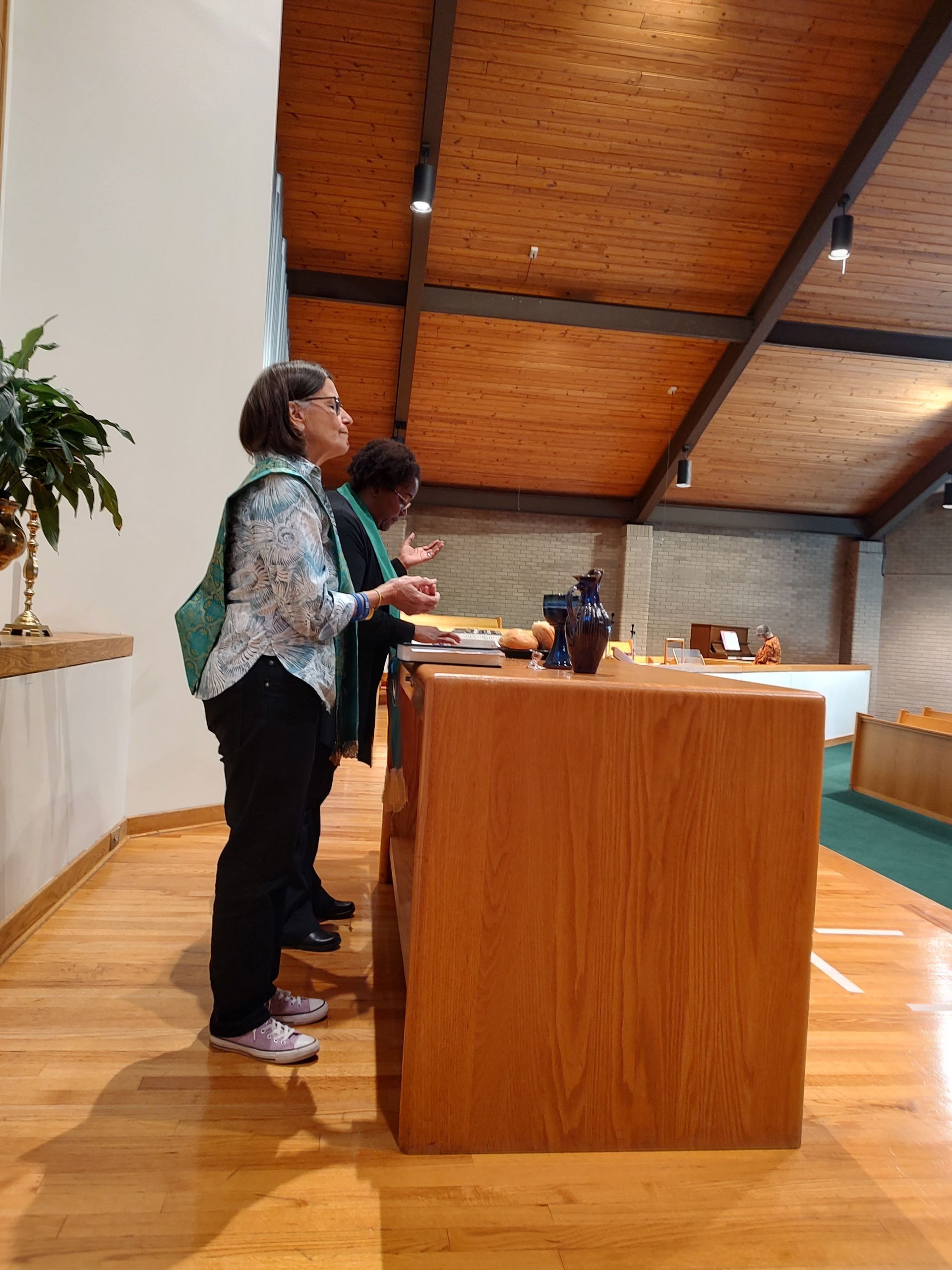 Two women at a wooden counter inside a church, looking upwards. Wood ceiling and flooring.