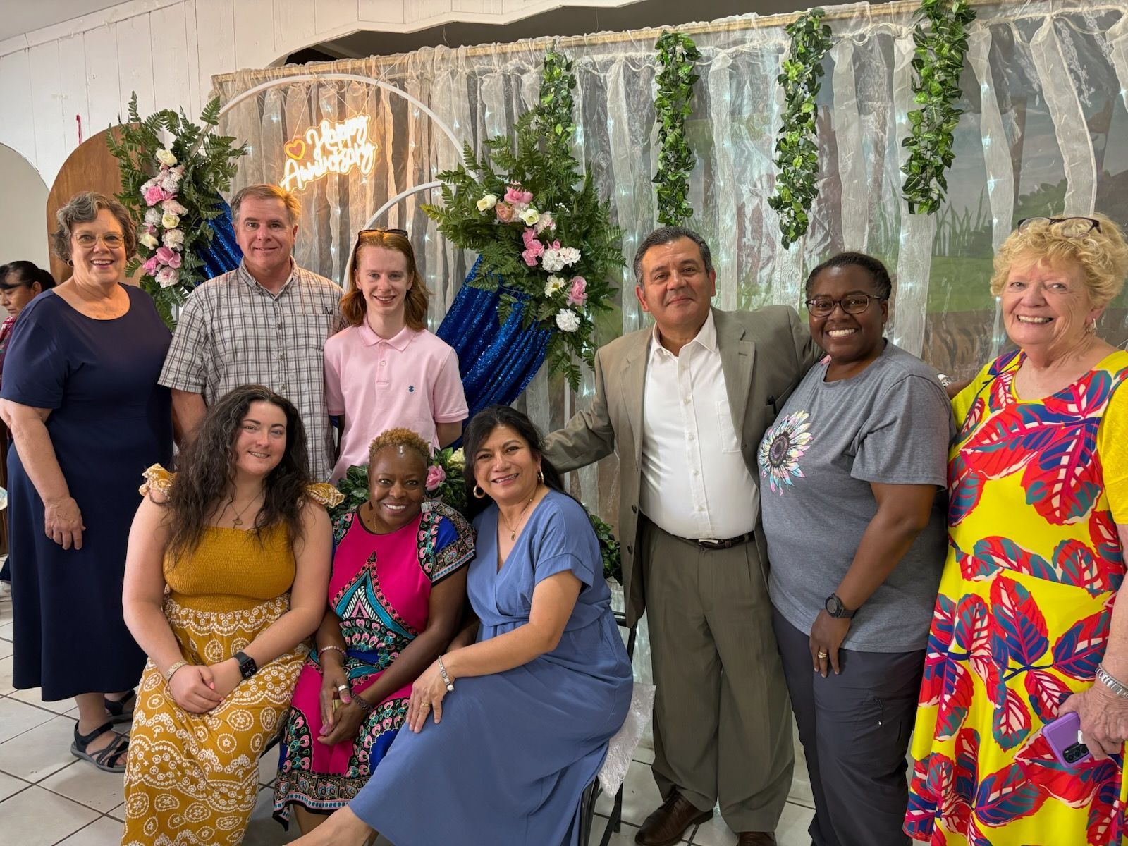 Group of people posing for a photo at an event with floral decorations, smiling.
