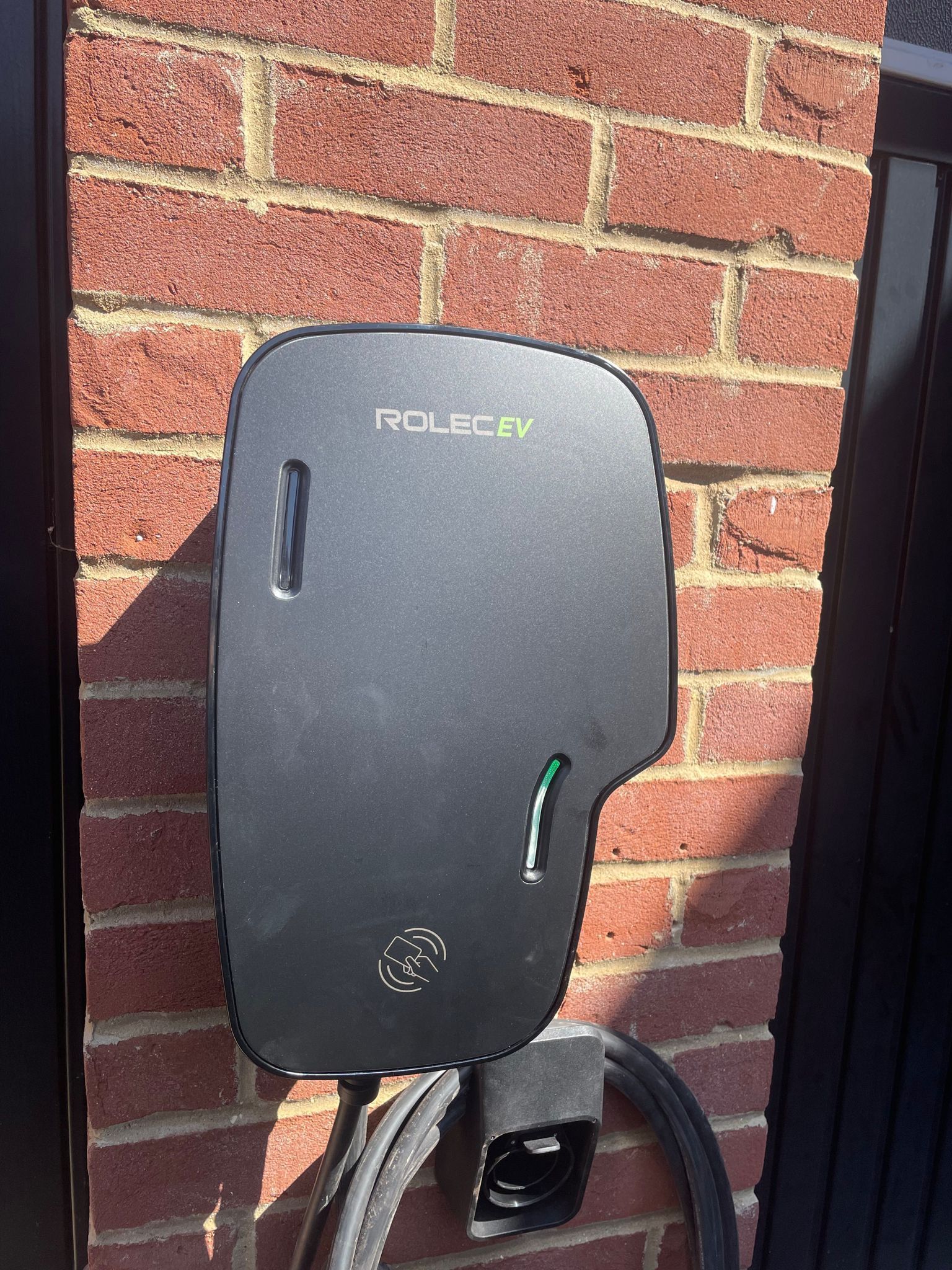 A black electric car charger is attached to a brick wall.