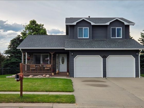 Two-story house with light siding, gray roof, two-car garage, and landscaped yard under a blue sky.