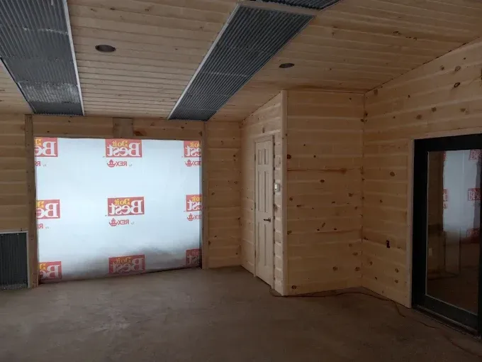 Interior room under construction with wood paneling, a doorway, and a large window covered in plastic.