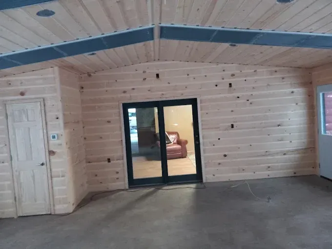 Interior with wood paneled walls, sliding glass door, and a closed door. Concrete floor.
